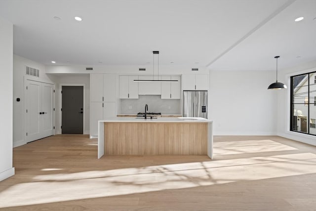 kitchen with sink, white cabinets, hanging light fixtures, stainless steel fridge with ice dispenser, and a center island with sink