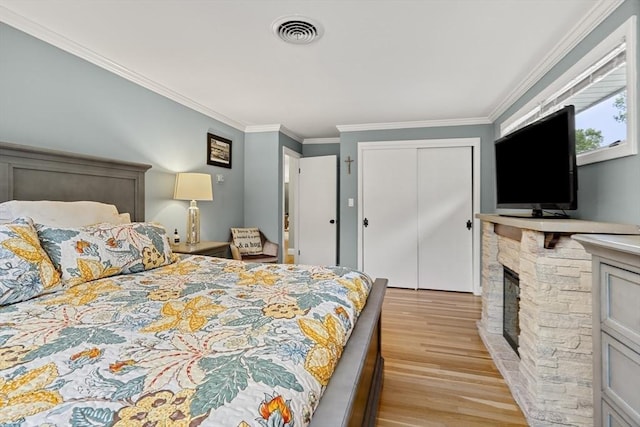 bedroom with light wood-style floors, ornamental molding, a closet, and a fireplace