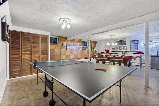 playroom with wooden walls, a textured ceiling, baseboard heating, a chandelier, and beamed ceiling
