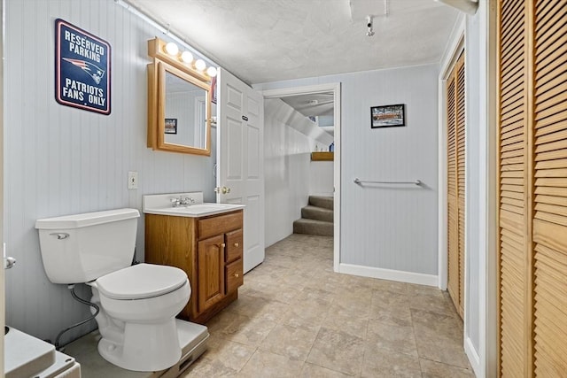 bathroom featuring a closet, toilet, vanity, and wood walls