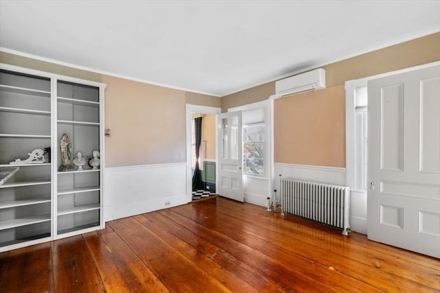 unfurnished room with hardwood / wood-style floors, radiator heating unit, and a wall mounted AC