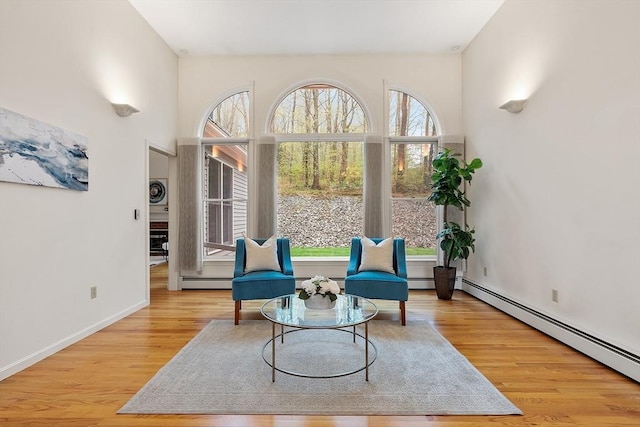 sitting room with wood finished floors, a baseboard heating unit, and baseboards