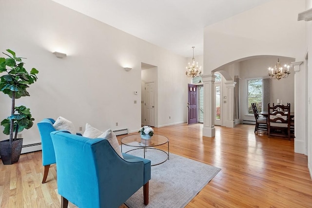 living area with a chandelier, arched walkways, decorative columns, light wood finished floors, and a baseboard radiator
