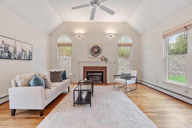 living area featuring vaulted ceiling, healthy amount of natural light, wood finished floors, a brick fireplace, and a ceiling fan