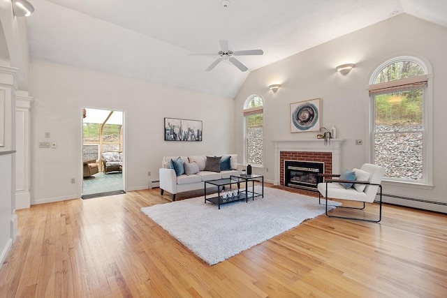 living area with vaulted ceiling, light wood finished floors, a brick fireplace, ceiling fan, and baseboard heating