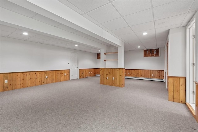 carpeted empty room featuring wainscoting, baseboard heating, wooden walls, and a paneled ceiling