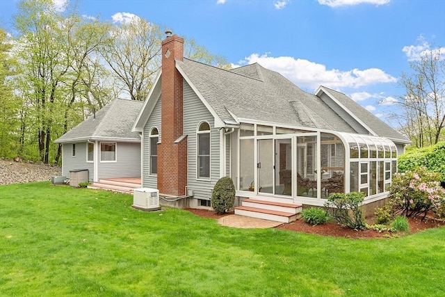 back of house with a sunroom, roof with shingles, a chimney, and a yard