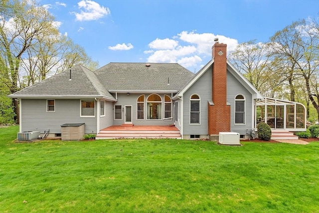 back of house featuring a chimney, a yard, a sunroom, and a shingled roof