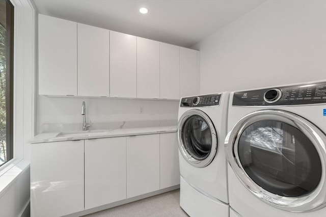 clothes washing area featuring cabinets, washing machine and dryer, and sink