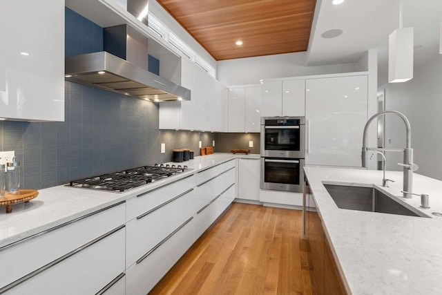 kitchen with sink, white cabinetry, appliances with stainless steel finishes, light stone countertops, and wall chimney range hood