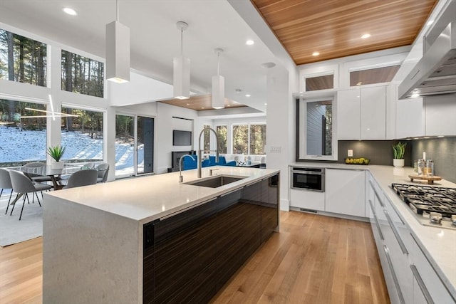 kitchen with wall chimney range hood, sink, white cabinetry, a kitchen island with sink, and wooden ceiling