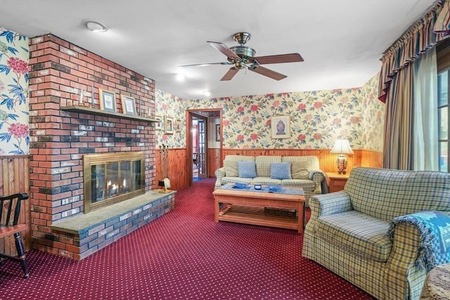 living room featuring ceiling fan, carpet flooring, wood walls, and a fireplace