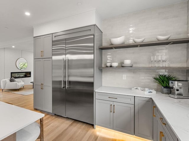 kitchen featuring built in refrigerator, gray cabinetry, light stone countertops, light wood-type flooring, and open shelves