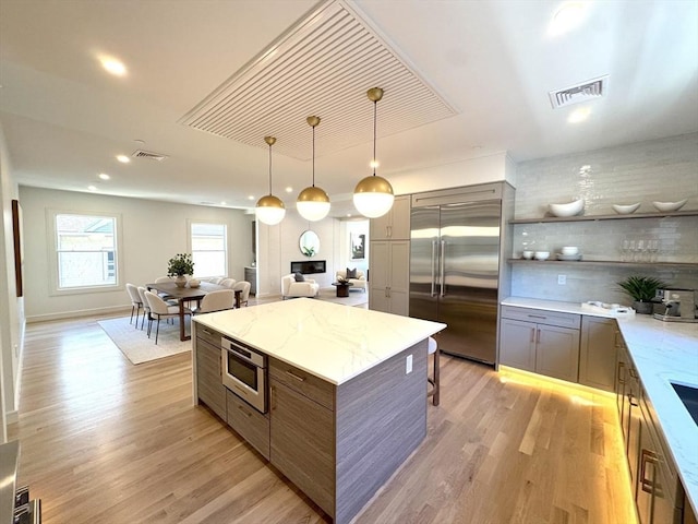 kitchen featuring built in appliances, light wood-style flooring, gray cabinets, a kitchen island, and light stone countertops