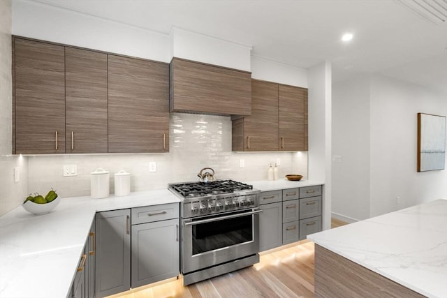 kitchen with stainless steel range, tasteful backsplash, light wood-style flooring, premium range hood, and recessed lighting