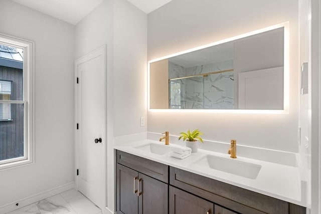 full bath featuring marble finish floors, a marble finish shower, double vanity, and baseboards