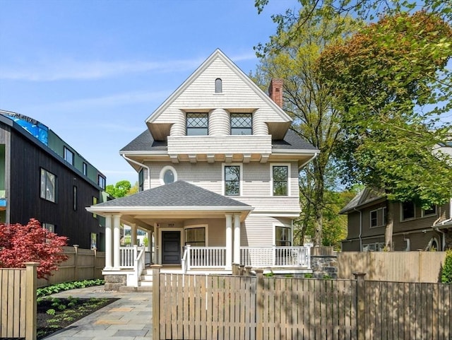 view of front of home featuring covered porch, a fenced front yard, a chimney, and roof with shingles