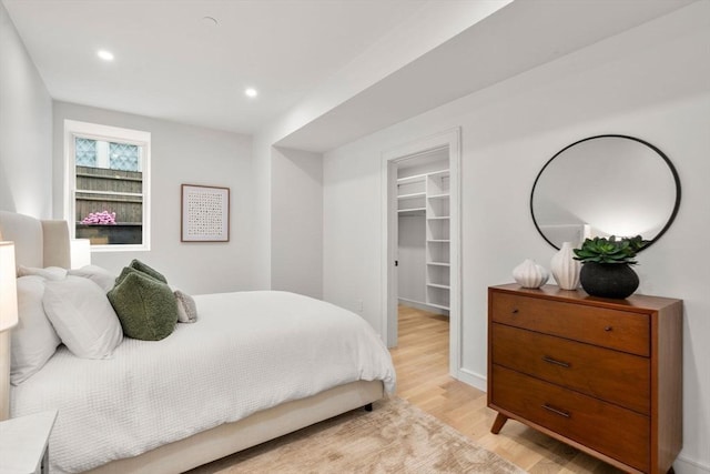bedroom featuring a walk in closet, light wood finished floors, recessed lighting, and a closet