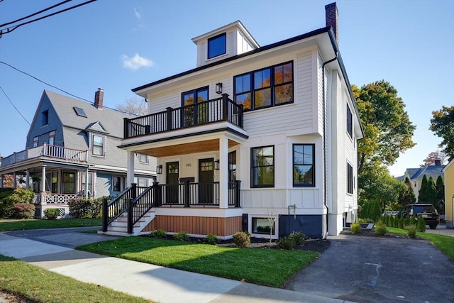 view of front of house with a chimney, covered porch, board and batten siding, a balcony, and a front lawn