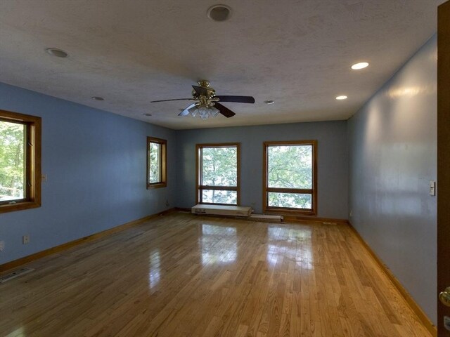 unfurnished room featuring light wood-type flooring, a textured ceiling, a healthy amount of sunlight, and ceiling fan