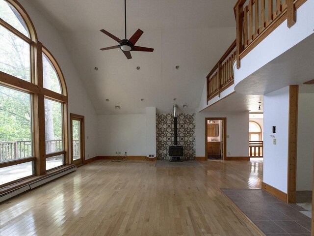 unfurnished living room featuring a wood stove, light hardwood / wood-style flooring, ceiling fan, and high vaulted ceiling