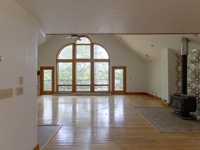 unfurnished living room with high vaulted ceiling, a wood stove, and light hardwood / wood-style flooring