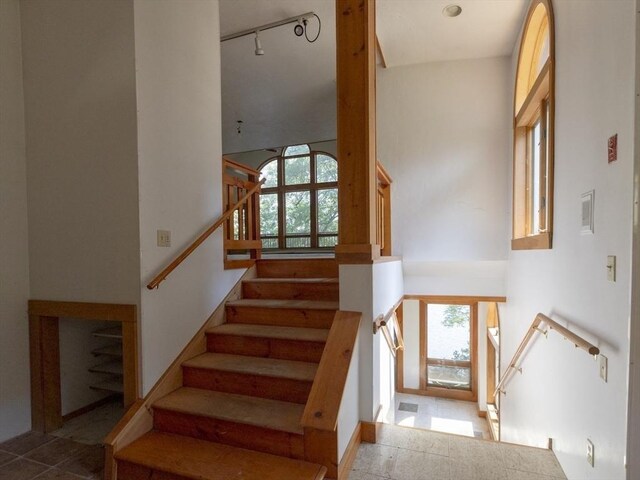 stairs featuring rail lighting, a high ceiling, and tile patterned floors