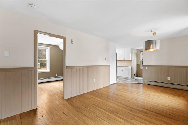 empty room with wainscoting, light wood-type flooring, and a baseboard radiator