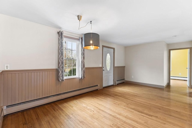 unfurnished room featuring a baseboard heating unit, a wainscoted wall, and light wood-type flooring