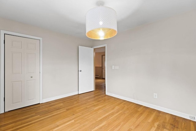 unfurnished bedroom featuring a baseboard heating unit, baseboards, and light wood finished floors