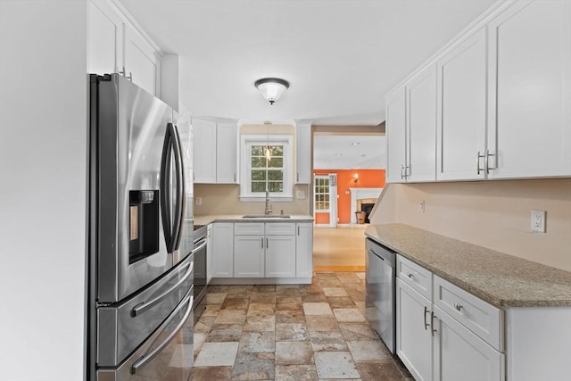 kitchen with stone finish floor, a sink, appliances with stainless steel finishes, white cabinets, and light stone countertops