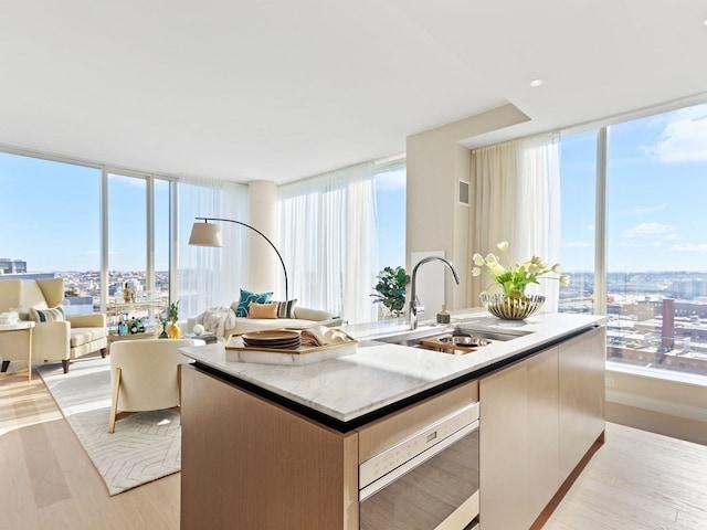 kitchen featuring a wall of windows, sink, a center island with sink, and light hardwood / wood-style flooring