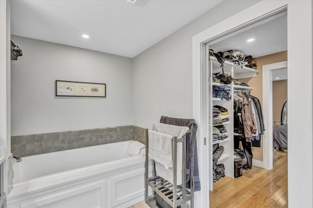 bathroom featuring a walk in closet, a bath, wood finished floors, and recessed lighting