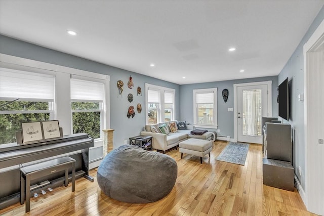 living area featuring light wood finished floors, baseboard heating, a healthy amount of sunlight, and recessed lighting