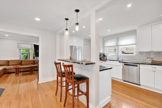 kitchen featuring stainless steel appliances, a sink, dark countertops, decorative backsplash, and light wood-style floors