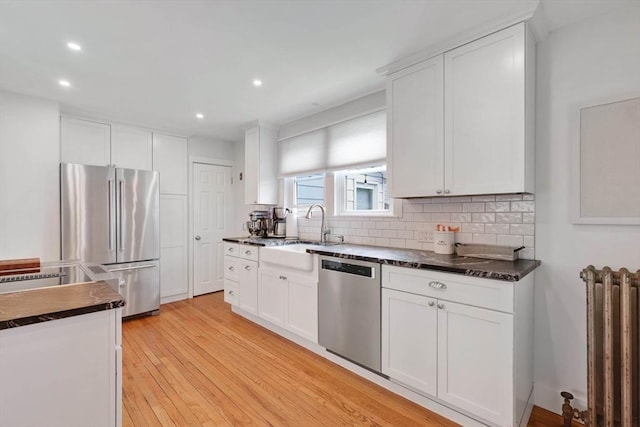 kitchen with appliances with stainless steel finishes, radiator heating unit, dark countertops, a sink, and backsplash