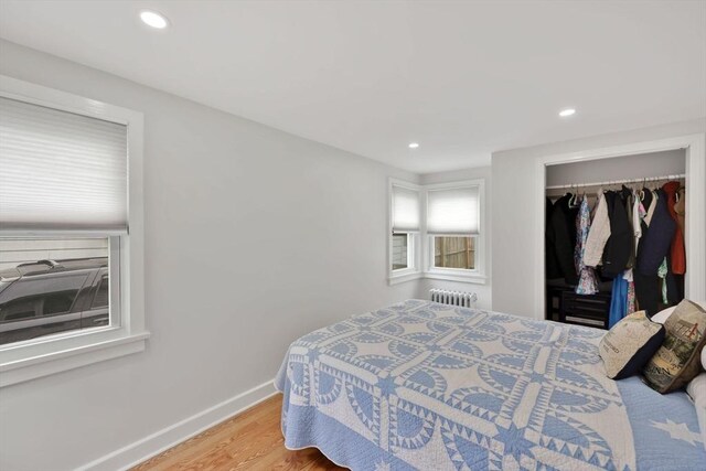 bedroom with radiator heating unit, recessed lighting, light wood-style flooring, baseboards, and a closet