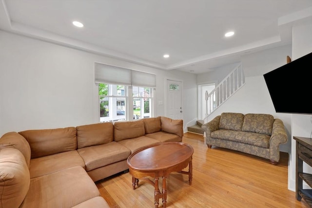 living room featuring light wood-type flooring, stairway, recessed lighting, and a raised ceiling