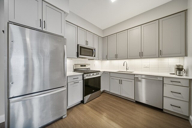 kitchen featuring sink, stainless steel appliances, light hardwood / wood-style flooring, gray cabinets, and decorative backsplash