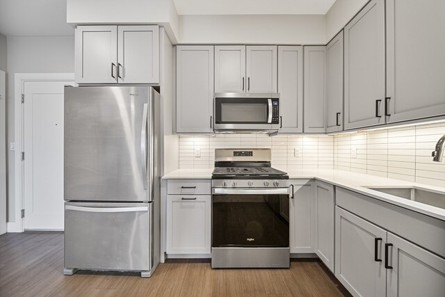 kitchen with gray cabinetry, sink, light hardwood / wood-style flooring, decorative backsplash, and appliances with stainless steel finishes