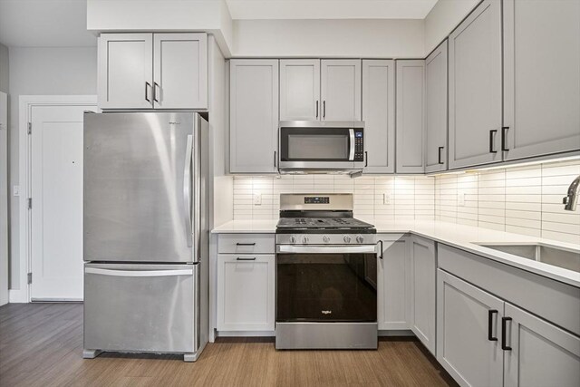 11 Walley St Unit 202, Boston, MA 02128 - kitchen with appliances with stainless steel finishes, gray cabinets, a sink, light wood finished floors, and tasteful backsplash