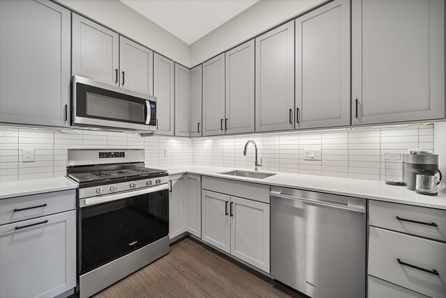 kitchen with appliances with stainless steel finishes, backsplash, dark hardwood / wood-style flooring, sink, and gray cabinets