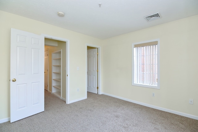 unfurnished bedroom with light carpet and a walk in closet