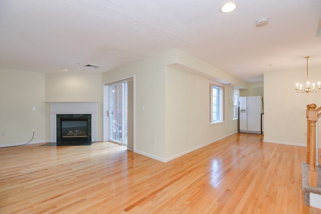 unfurnished living room with light hardwood / wood-style floors, a textured ceiling, and an inviting chandelier