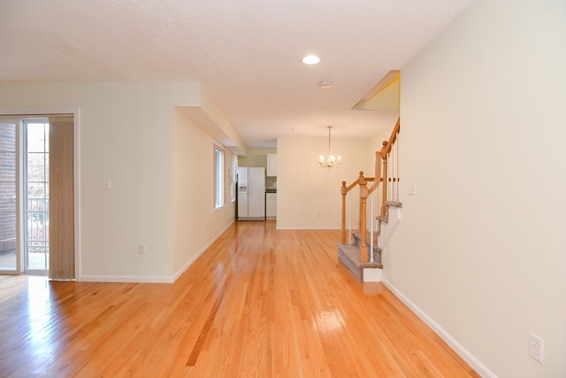 hall featuring a notable chandelier, a textured ceiling, and light wood-type flooring