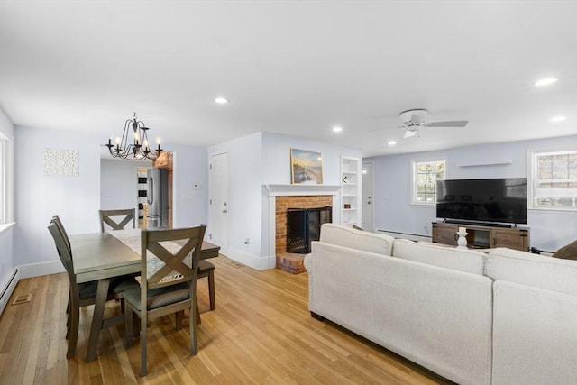 living room featuring a brick fireplace, ceiling fan with notable chandelier, built in features, and light hardwood / wood-style floors