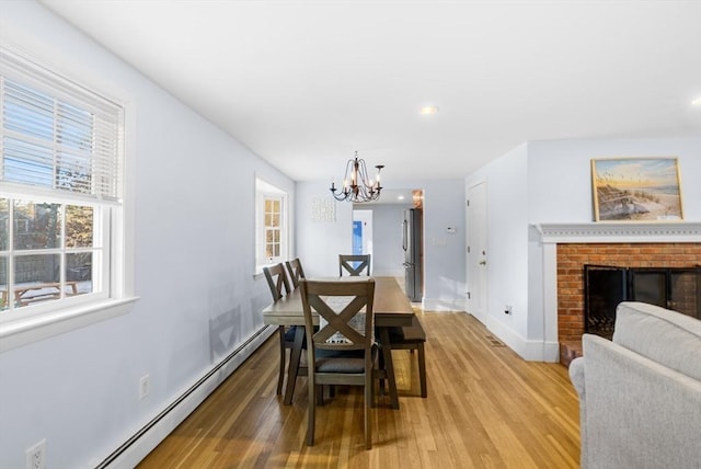 dining room with an inviting chandelier, a brick fireplace, wood-type flooring, and baseboard heating