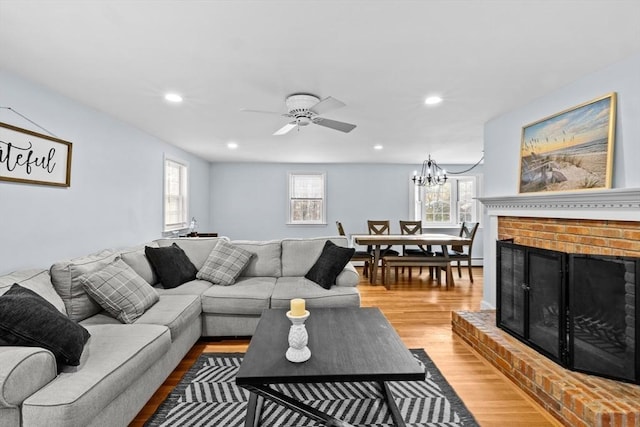 living room with a brick fireplace, ceiling fan with notable chandelier, and light wood-type flooring