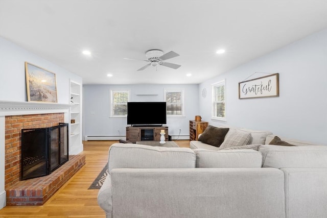 living room with a baseboard heating unit, ceiling fan, light hardwood / wood-style floors, a brick fireplace, and built in shelves