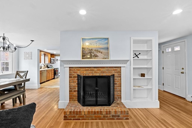 living room featuring sink, a chandelier, a brick fireplace, light hardwood / wood-style flooring, and built in features